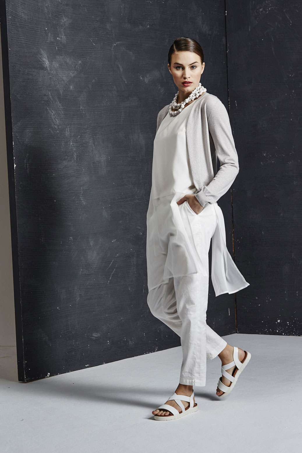 This model wears a two-layered long vest in silk with a mini cardigan in lamé and linen trousers